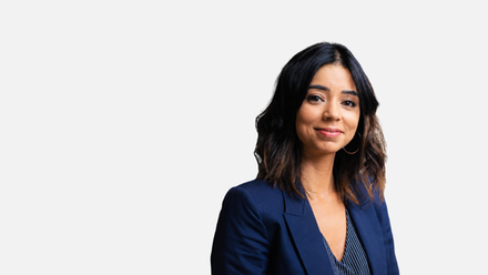 A profile photo of Kam Mayne, wearing a navy blazer against a plain grey background