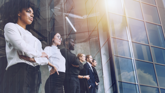 A diverse group of professionals standing together, looking ahead through the glass exterior of a modern office building