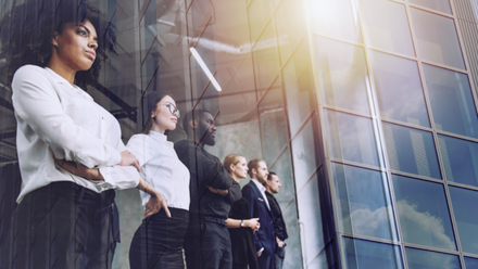 A diverse group of professionals standing together, looking ahead through the glass exterior of a modern office building