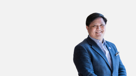 Portrait of Alex Gapud wearing a blue suit and shirt smiling to camera.