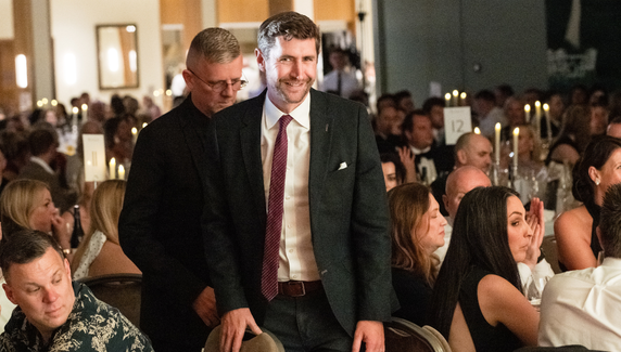  A smiling guest walks through a crowded awards dinner venue.